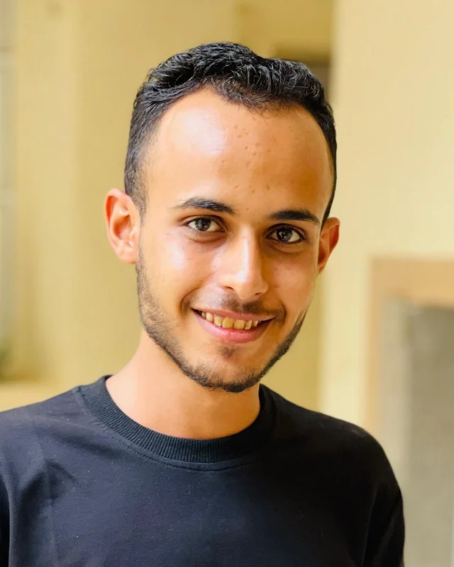 Portrait of Muneeb Almoliky, smiling, in a sunlit corridor.